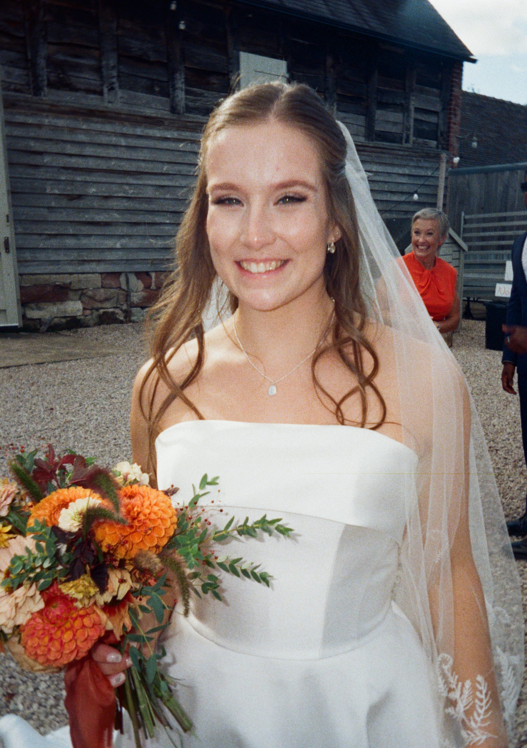 Film photo of a smiling bride with her veil and a bouquet of orange flowers