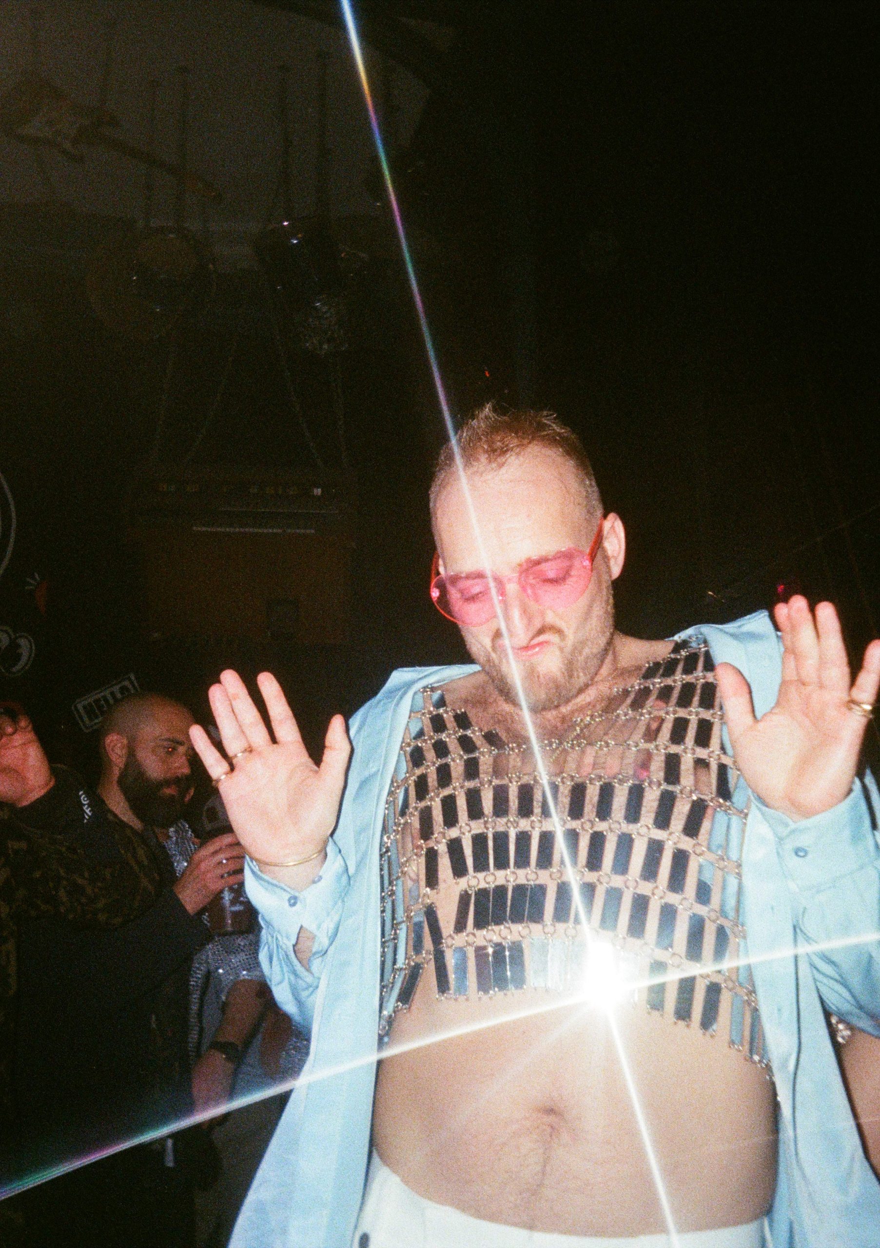 Film photo of a guest in pink sunglasses and a mesh top caught in the camera flash, hands up