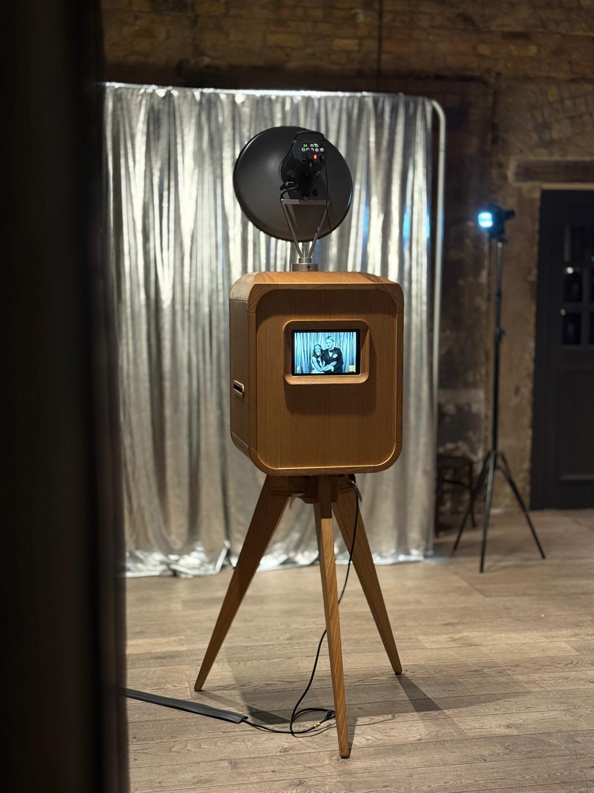 The FLASH BSTRDS! booth: a wooden mid-century cabinet on tapered legs with a round flash on top, in front of a silver curtain
